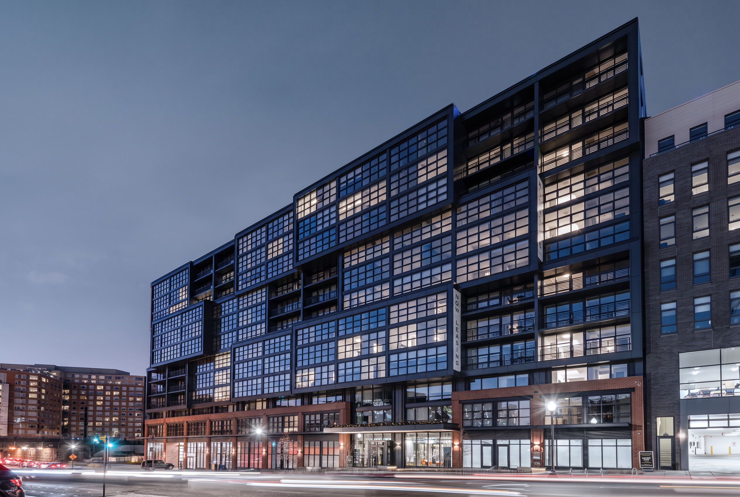 Contemporary residential building with steel-framed glass facade and street-level retail at dusk